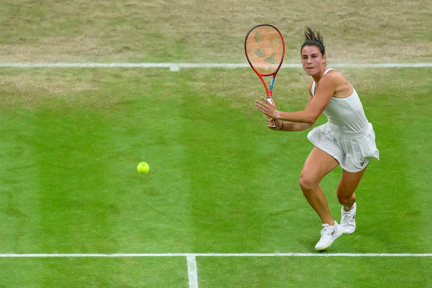 Female tennis player poised for a backhand shot at Wimbledon.