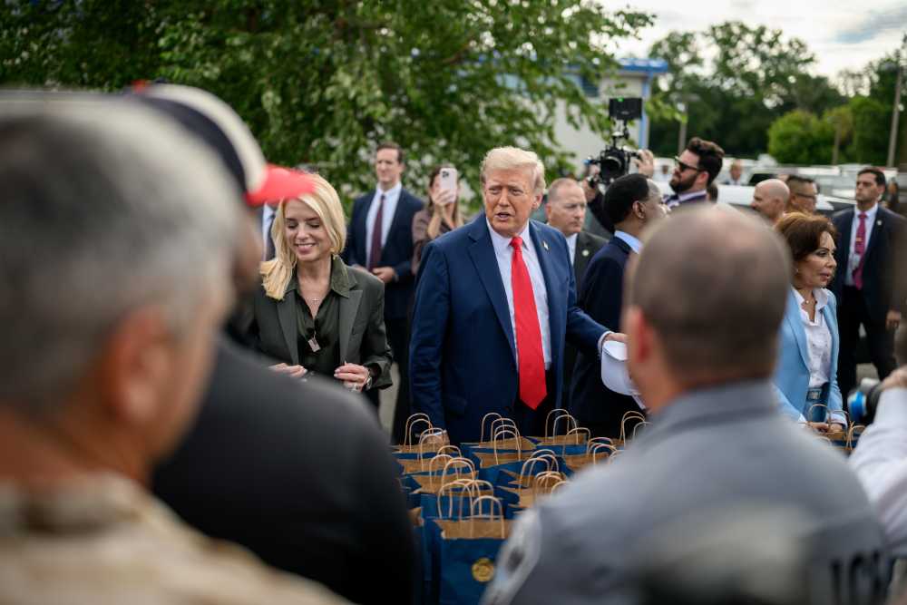 President Donald Trump wearing a blue suit and red tie walks outdoors with aides and security personnel, with gift bags visible in the foreground.