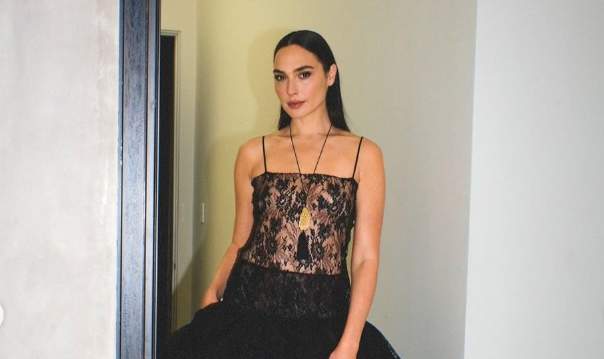 Gal Gadot in a black lace dress with sheer bodice at a Snow White premiere, styled with statement jewelry, hair, makeup, and nails credited in caption