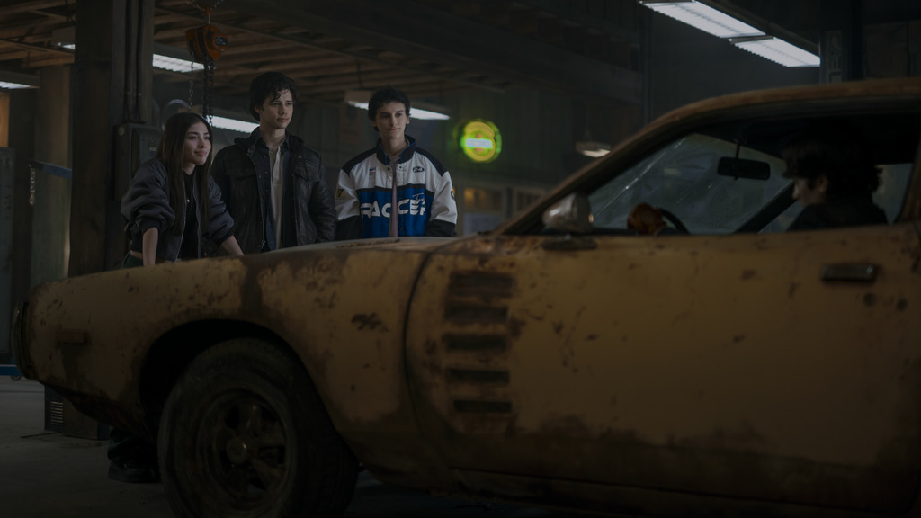Three teenagers stand looking at a damaged yellow car in a garage in a scene from the canceled Prime Video series "Motorheads"