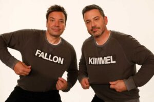 Jimmy Fallon and Jimmy Kimmel posing together wearing matching dark gray sweaters with their last names "FALLON" and "KIMMEL" printed in white text across the front.