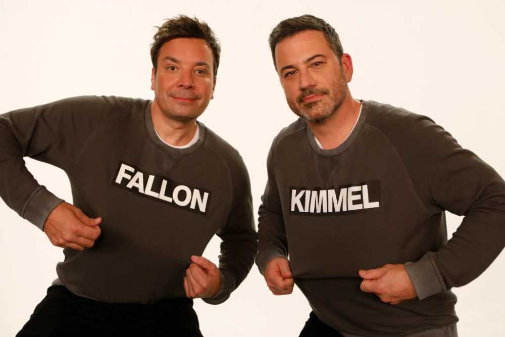 Jimmy Fallon and Jimmy Kimmel posing together wearing matching dark gray sweaters with their last names "FALLON" and "KIMMEL" printed in white text across the front.