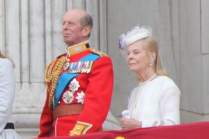 The Duke and Duchess of Kent standing on the balcony of Buckingham Palace during the Trooping the Colour ceremony in June 2013, with the Duke wearing his ceremonial military uniform with medals and the Duchess in a white outfit.