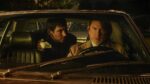 Daniel Craig as detective Benoit Blanc and Josh O'Connor as Father Jud Duplenticy sitting in a vintage car at night, illuminated by dim lighting, creating a tense atmosphere characteristic of the film's Gothic elements.