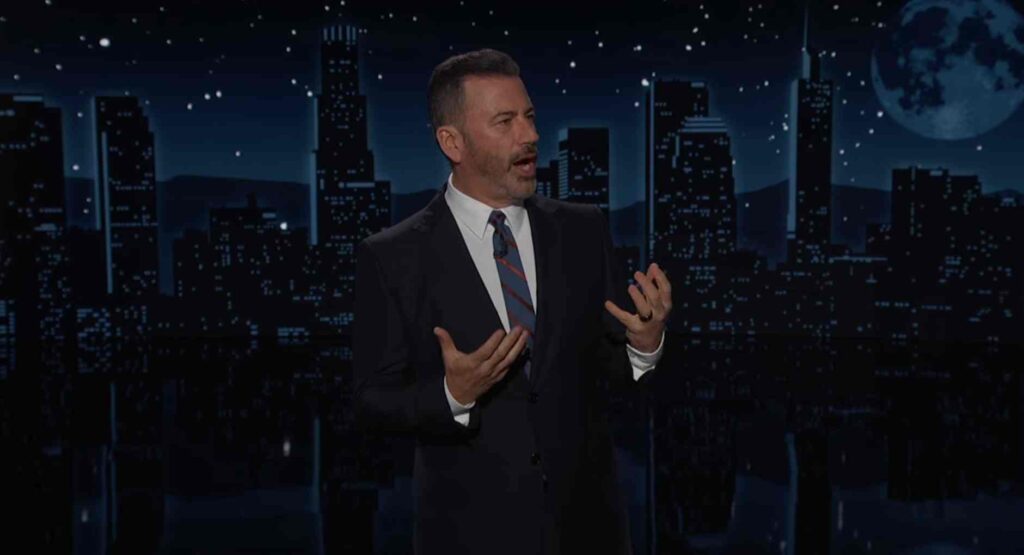 Jimmy Kimmel delivering a monologue on his late-night show set with a nighttime city skyline backdrop, gesturing with both hands while discussing President Trump's visit to England.