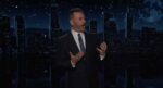Jimmy Kimmel delivering a monologue on his late-night show set with a nighttime city skyline backdrop, gesturing with both hands while discussing President Trump's visit to England.