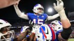 Buffalo Bills quarterback Josh Allen celebrates with raised arms while being lifted by teammates after leading a comeback victory, wearing blue jersey number 15 in a packed stadium
