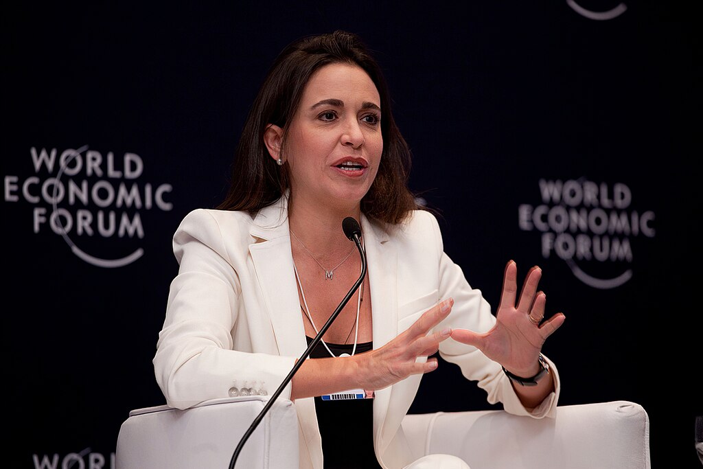 María Corina Machado speaking at the World Economic Forum panel with microphone and WEF backdrop