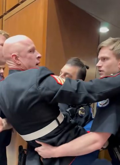 U.S. Capitol Police officers escort Marine veteran and Senate candidate Brian McGinnis out of a Senate Armed Services hearing room after he protested U.S. military actions related to Iran while Sen. Tim Sheehy assisted officers.
