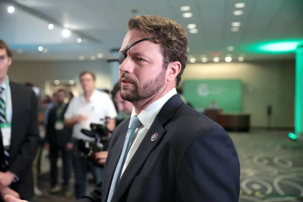 U.S. Representative Dan Crenshaw speaking with attendees at the American Conservative Coalition Summit in Washington, D.C., wearing a suit and signature eye patch.