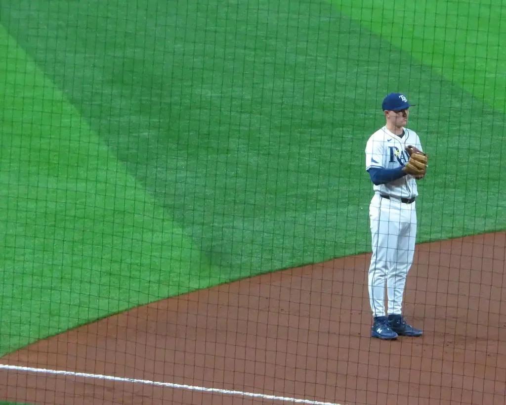 Curtis Mead in Tampa Bay Rays uniform holding baseball glove in ready position against the green outfield wall at Tropicana Field.