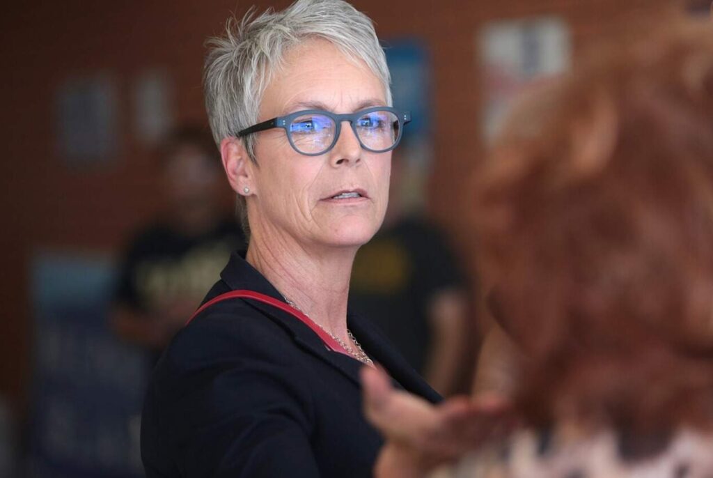 Jamie Lee Curtis wearing blue-framed glasses and dark clothing, professional headshot photographed at Peoria, Arizona location.