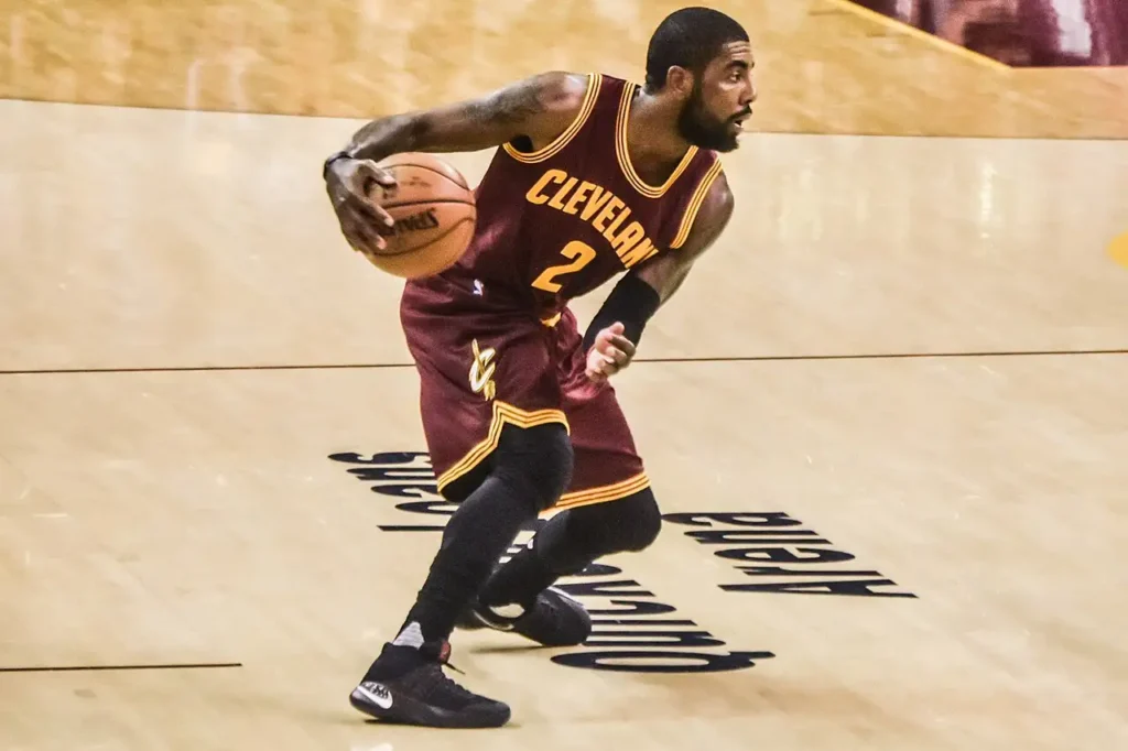 Kyrie Irving in Cleveland Cavaliers #2 maroon jersey dribbling basketball during game action at Quicken Loans Arena, with crowd visible in background.