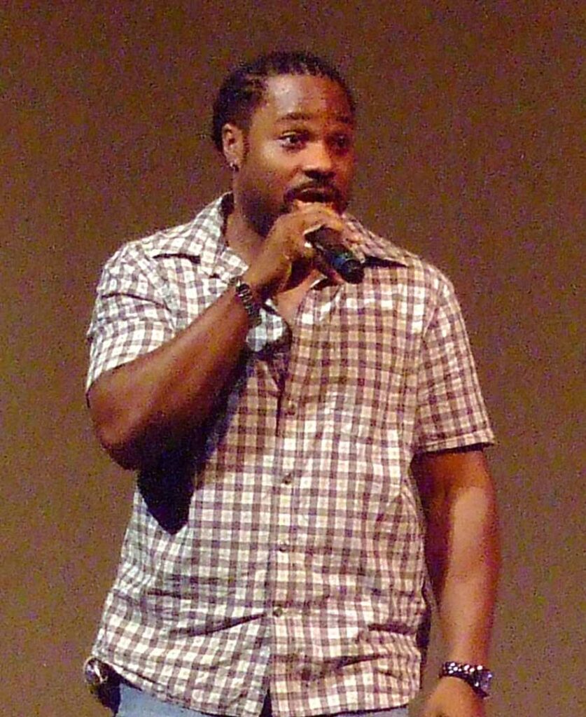Portrait of actor Malcolm-Jamal Warner smiling in a dark sweater against a plain background.