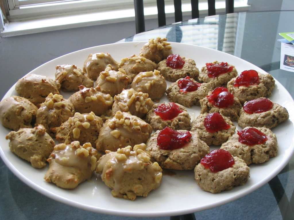 A plate of maple spice cookies and thumbprint cookies arranged on a cooling rack, with a blurred kitchen background. (CC BY-SA 4.0)