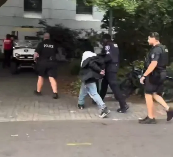 Multiple police officers and emergency responders at Seattle Center incident scene, with visible suspect being apprehended near public facility during daytime.