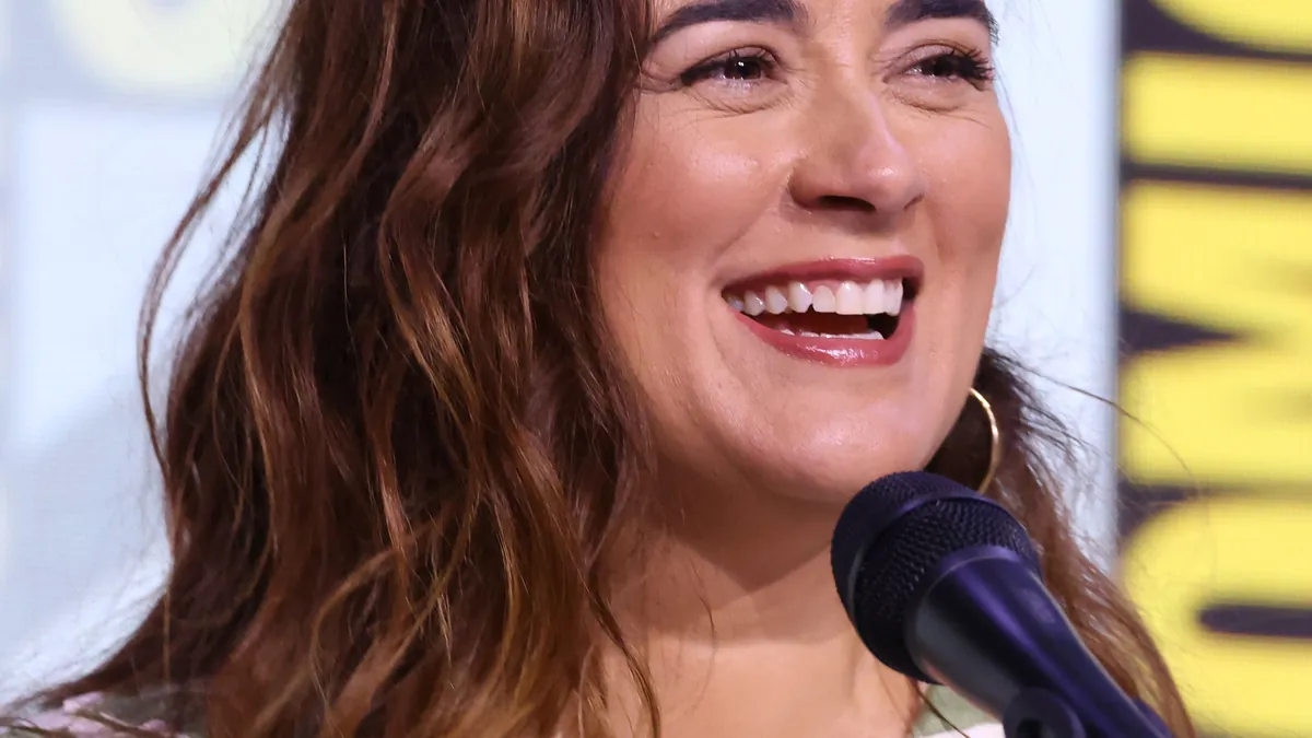 Cote de Pablo speaking into a microphone during an entertainment panel.