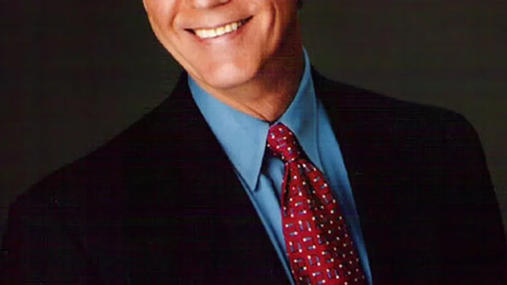Actor Alan Dysert posing in a dark suit jacket and open collar shirt for an official portrait.