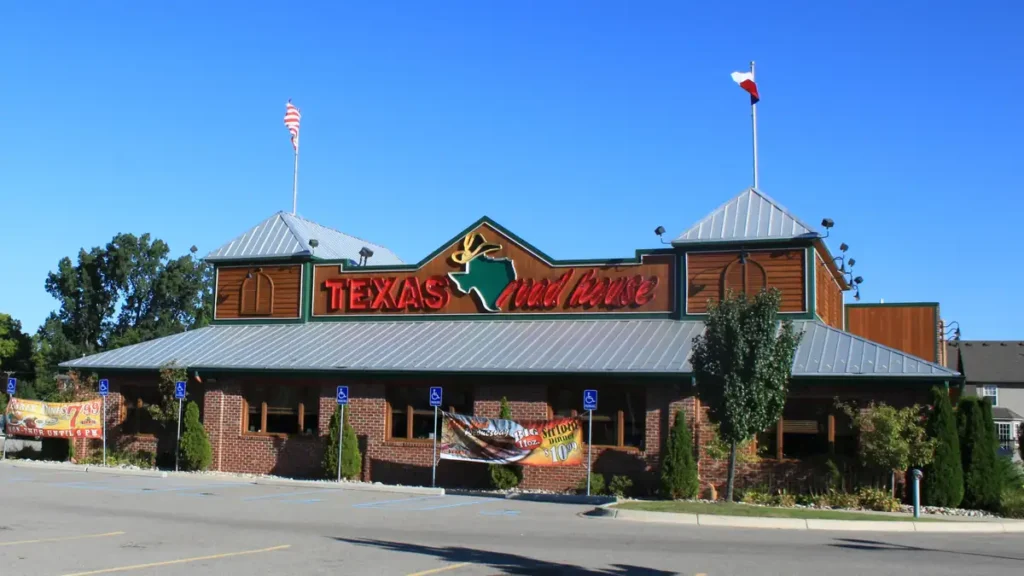Exterior view of a Texas Roadhouse restaurant building with rustic timber siding under daylight.